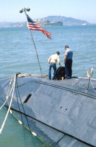 men standing over an open hatch of a submarine