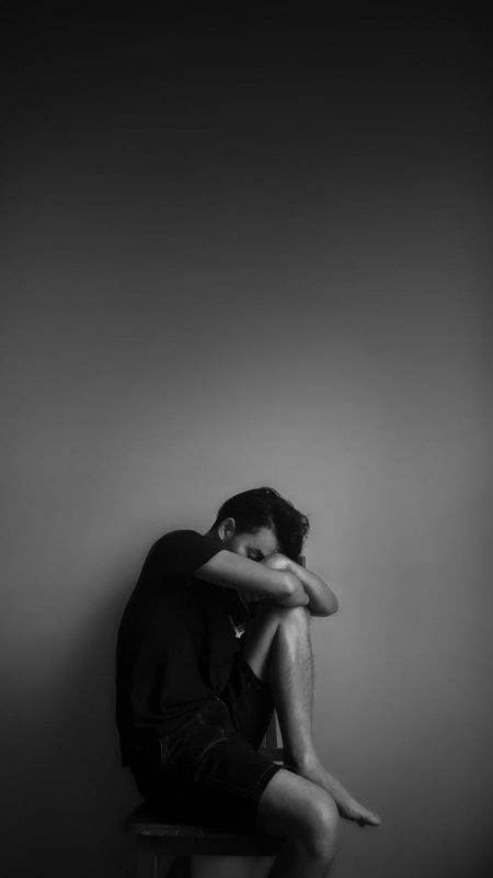 grayscale photography of man sitting beside wall