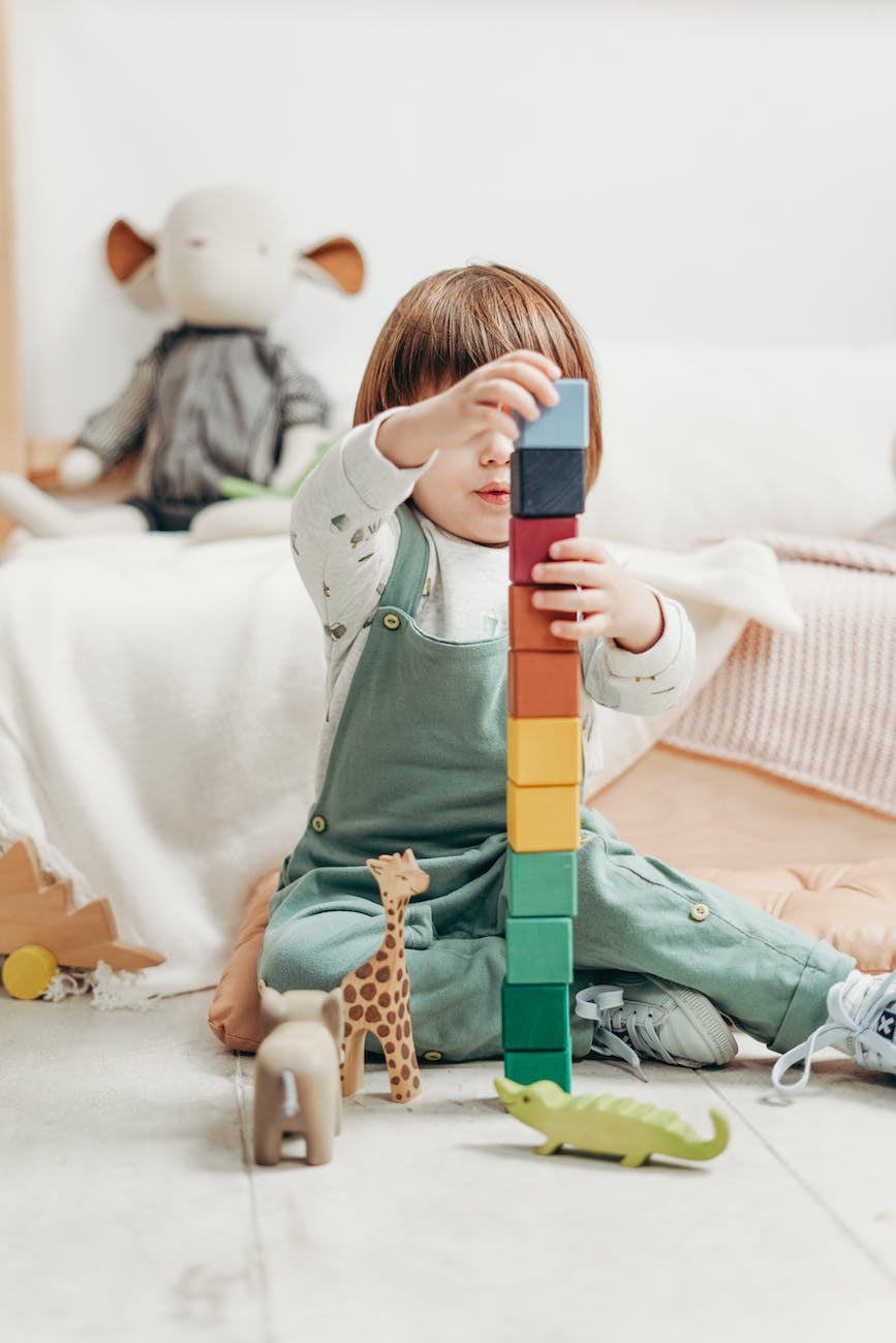 child in white long sleeve top and dungaree trousers playing with lego blocks