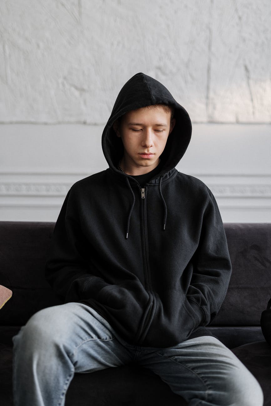 Hard noise in the teenage years man in black hoodie sitting on brown couch