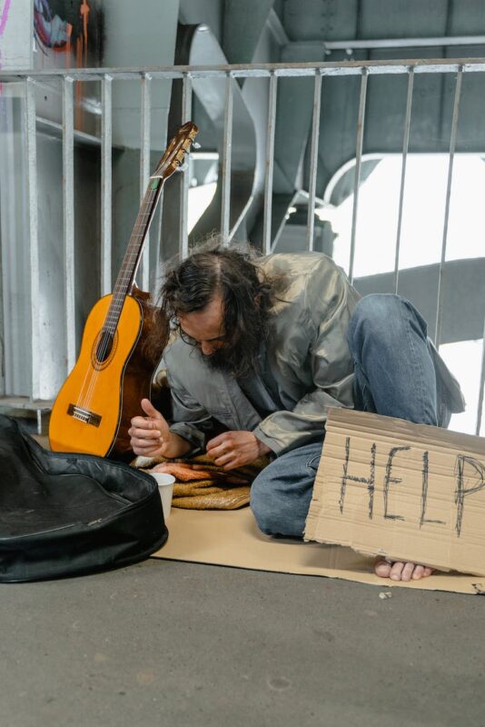 a beggar sitting on the street near metal fence